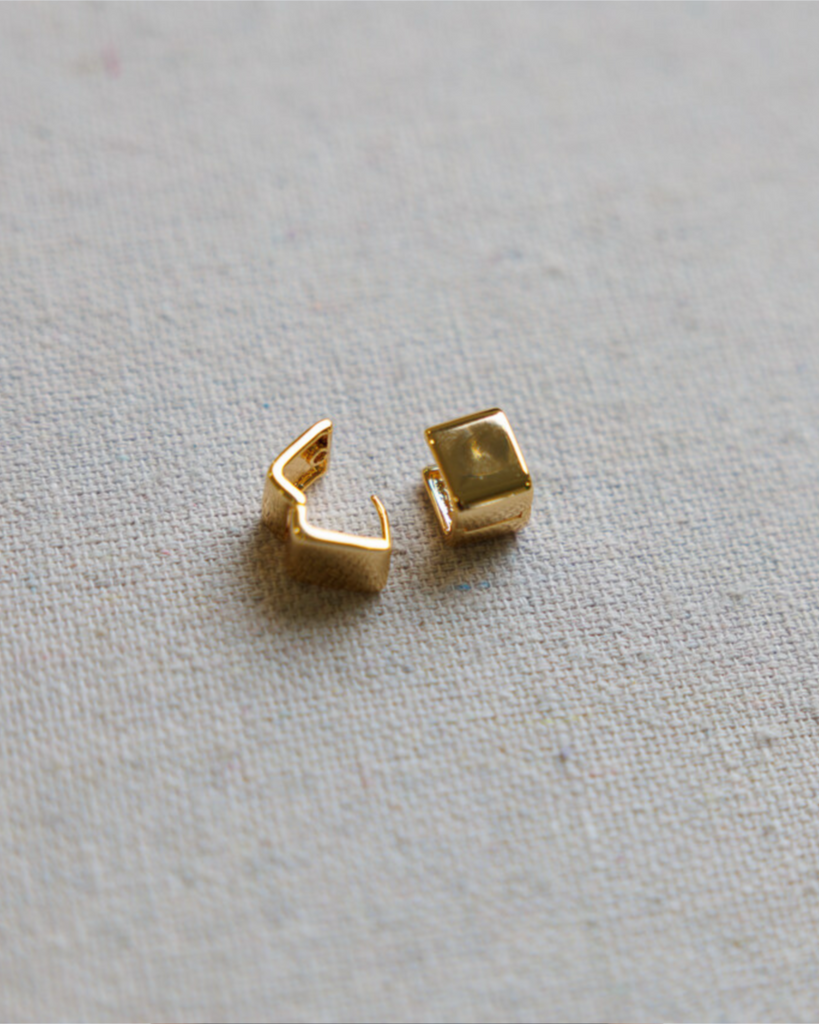 Two gold square hoop earrings on a textured gray background