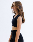 Woman wearing a black cropped layering top and black pants on a white background