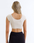Woman wearing a nude cropped layering top and black pants on a white background