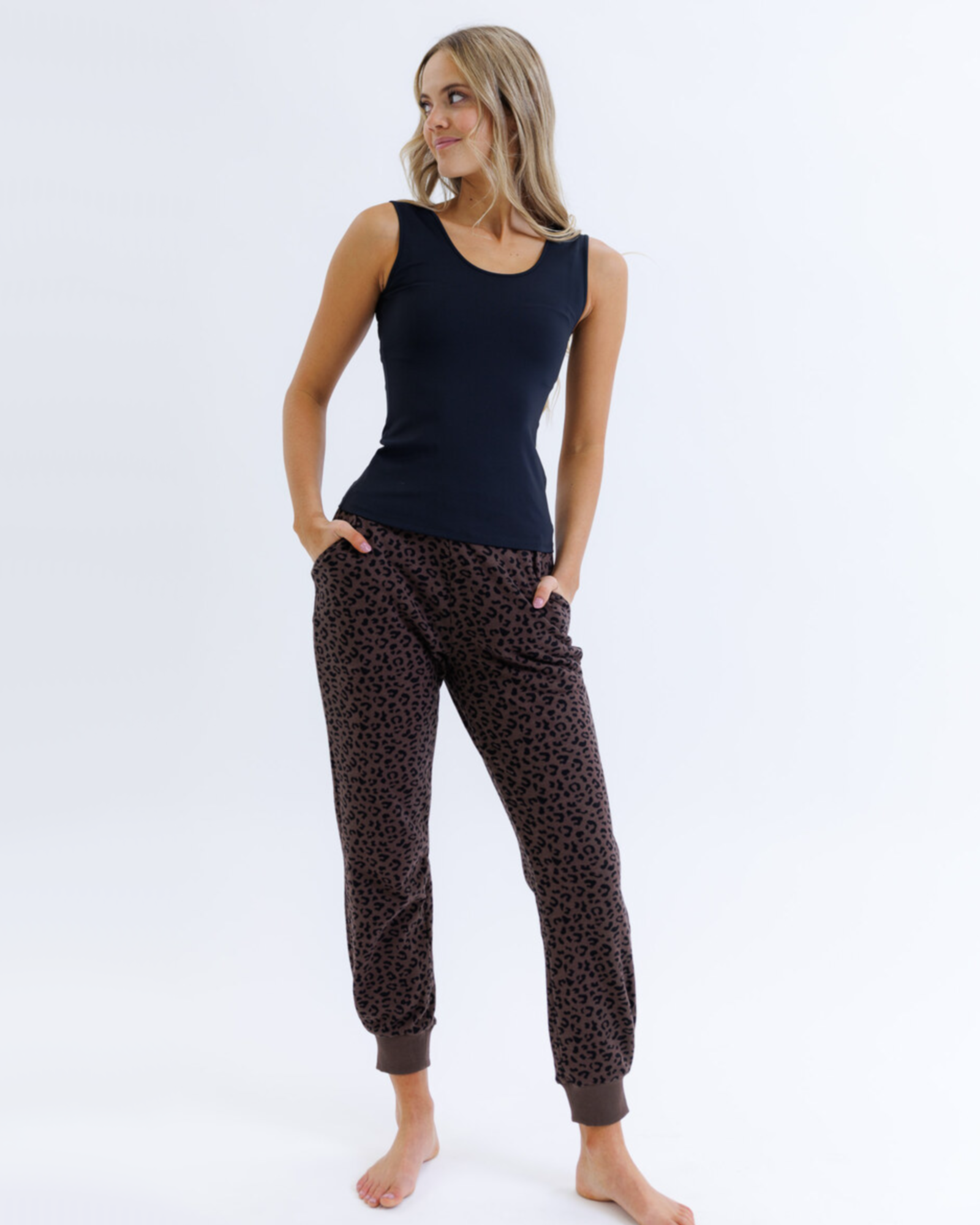 Woman wearing a black layering tank top and brown animal print pants against a white background