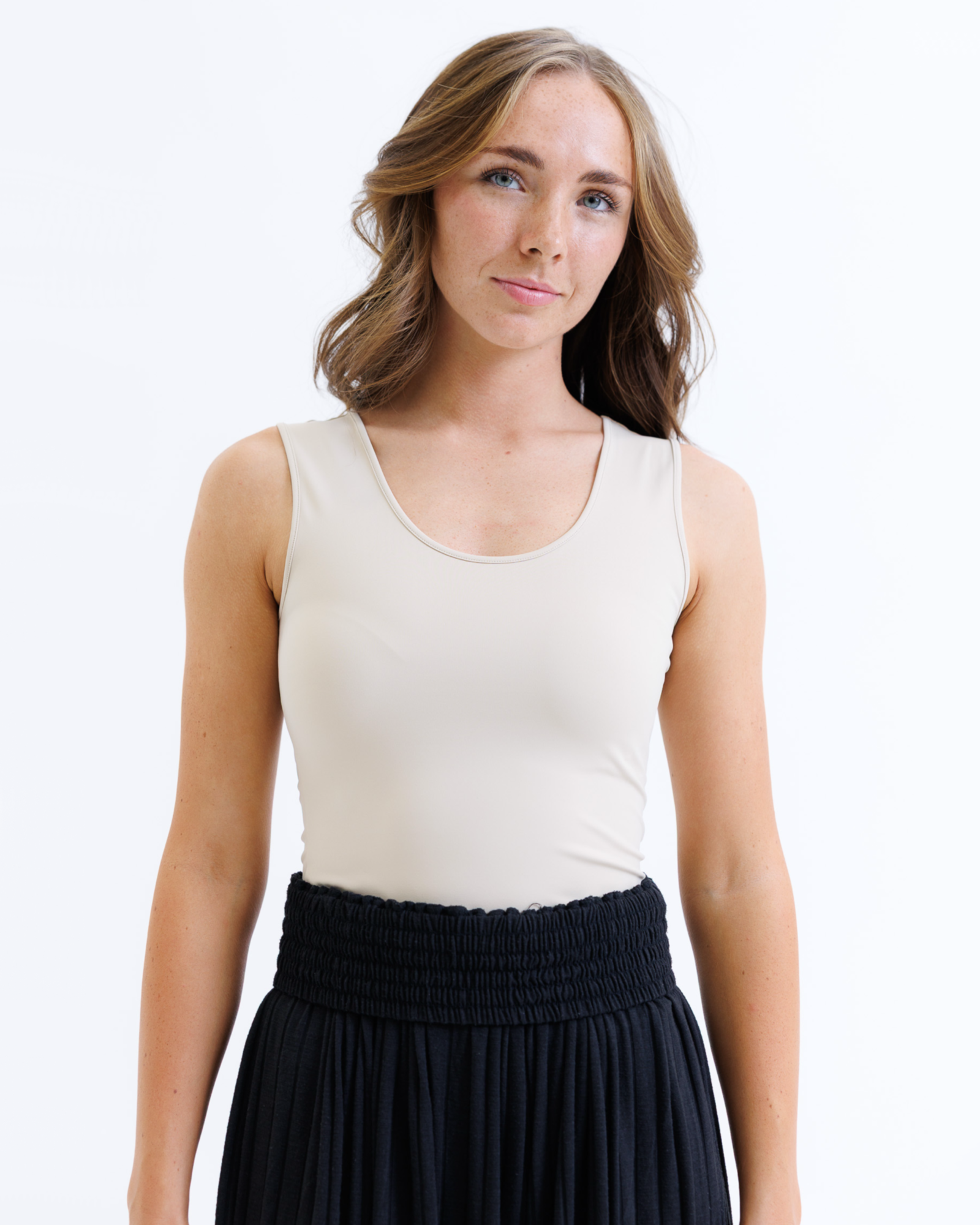 Woman wearing a nude layering tank top and black skirt on a white background