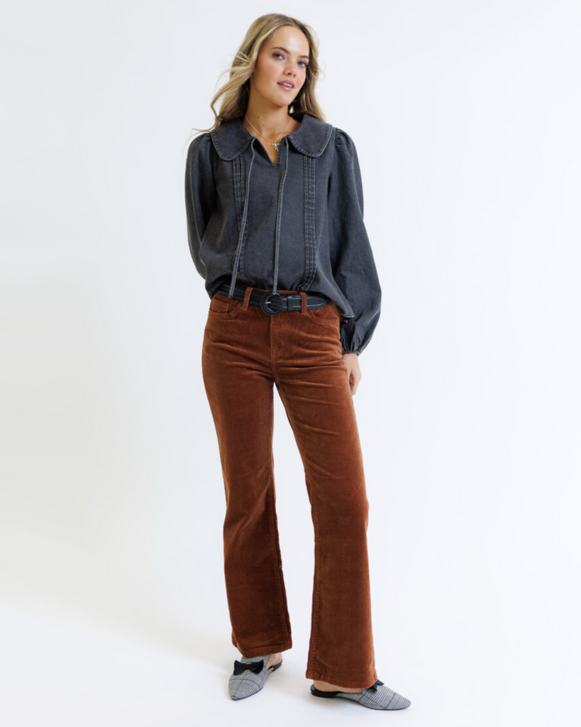 Woman wearing a dark denim blouse and brown corduroy jeans on a white background