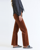 Woman wearing a dark denim blouse and brown corduroy jeans on a white background