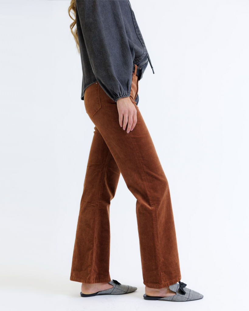 Woman wearing a dark denim blouse and brown corduroy jeans on a white background