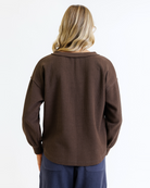 Woman wearing a brown long-sleeve top and navy pants on a white background