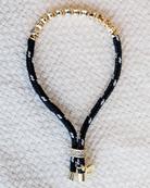 Black paracord bracelet with gold beads on a textured beige surface