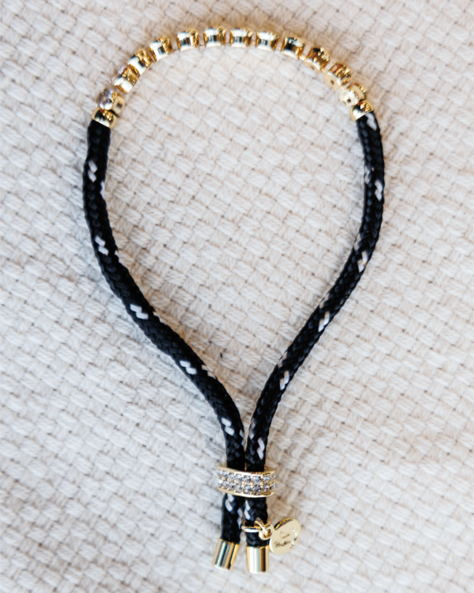Black paracord bracelet with gold beads on a textured beige surface