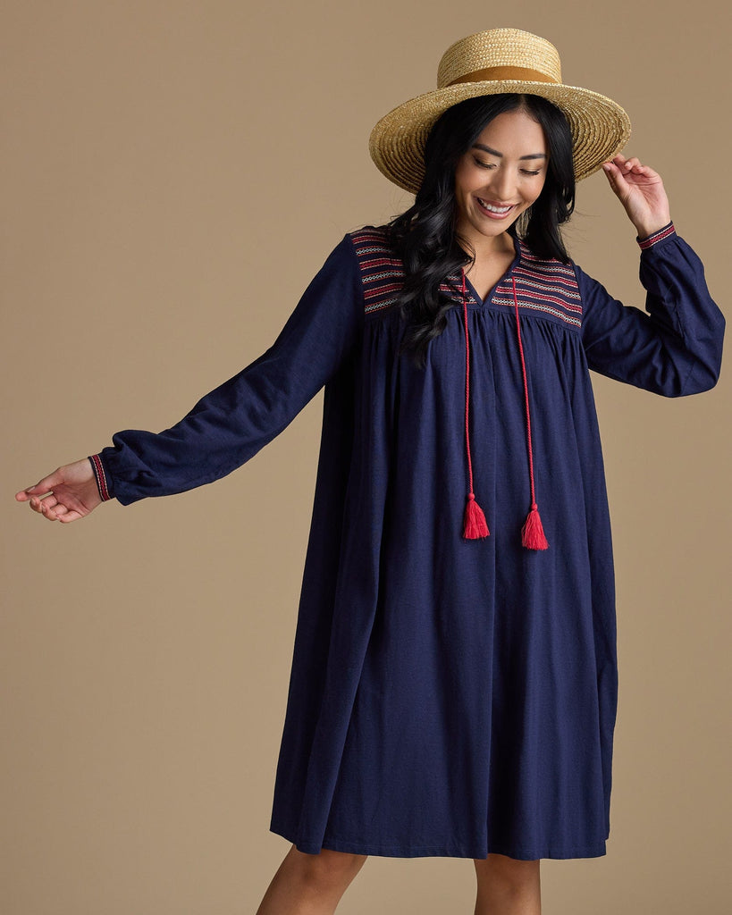 Woman in a long sleeve, knee-length, navy dress with red tassels