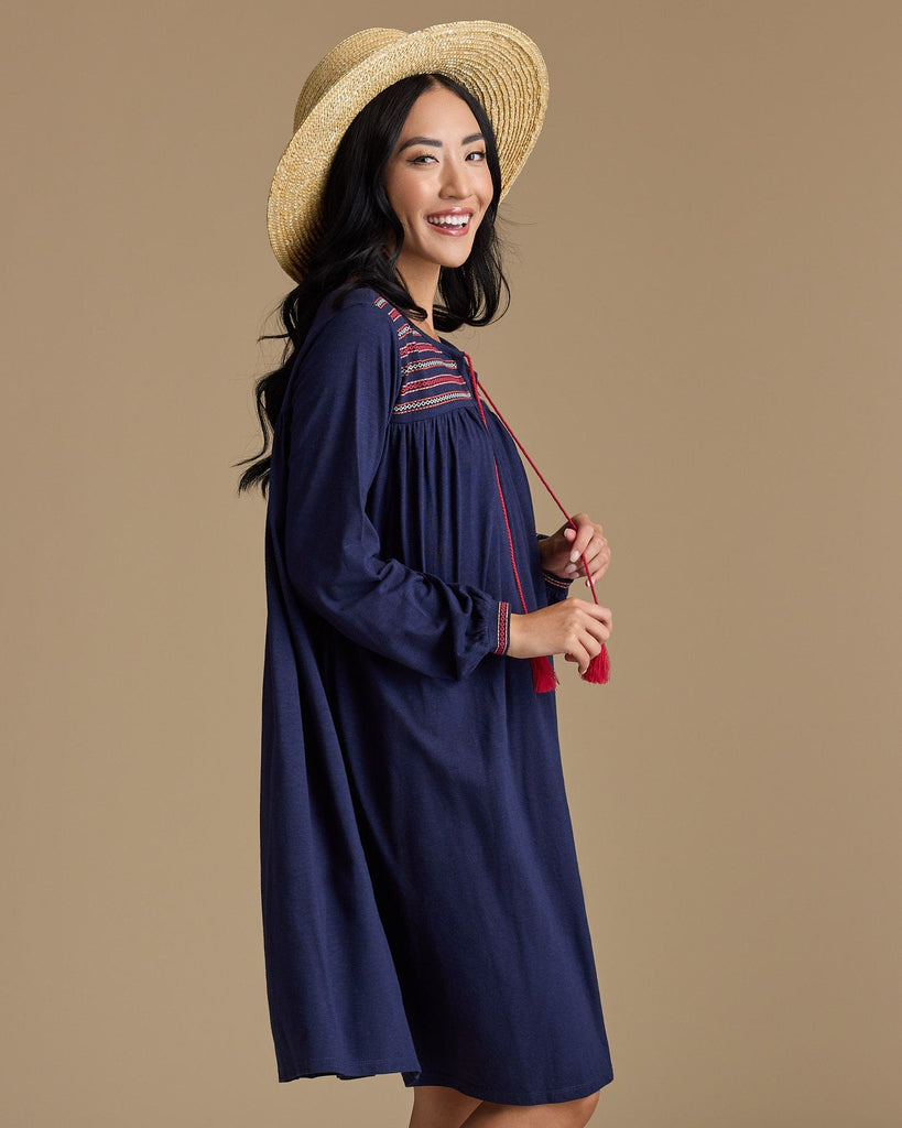 Woman in a long sleeve, knee-length, navy dress with red tassels