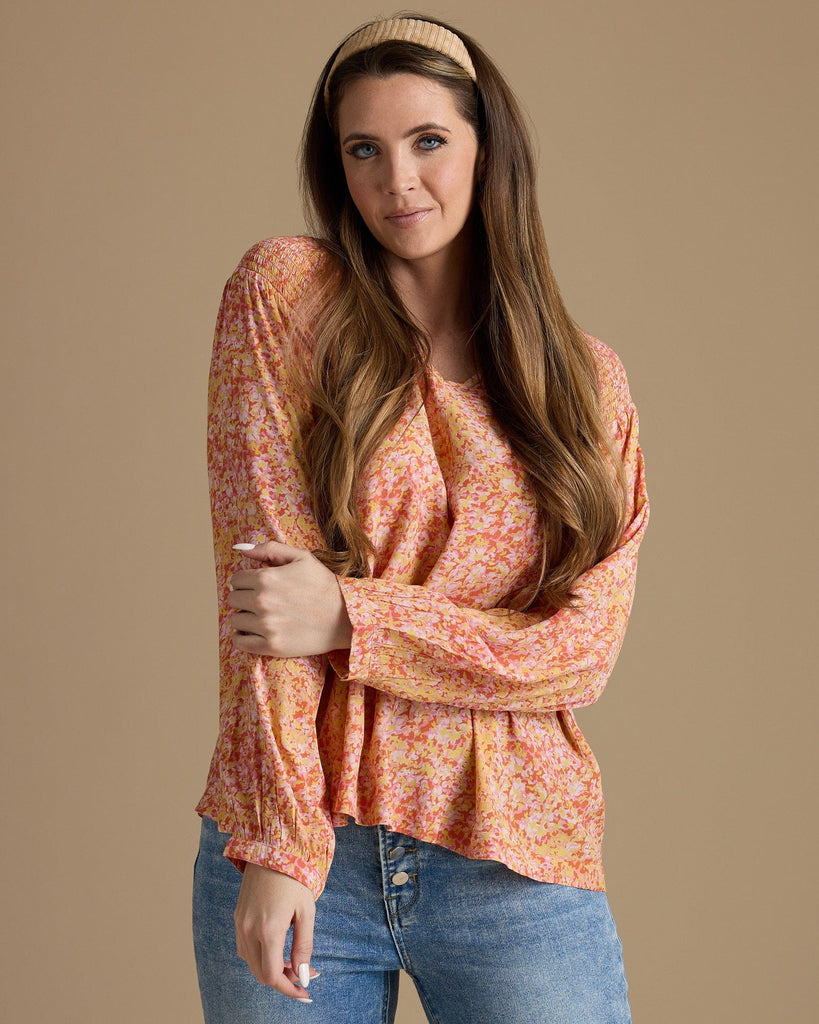 Woman in an orange, yellow and pink blouse with long sleeves