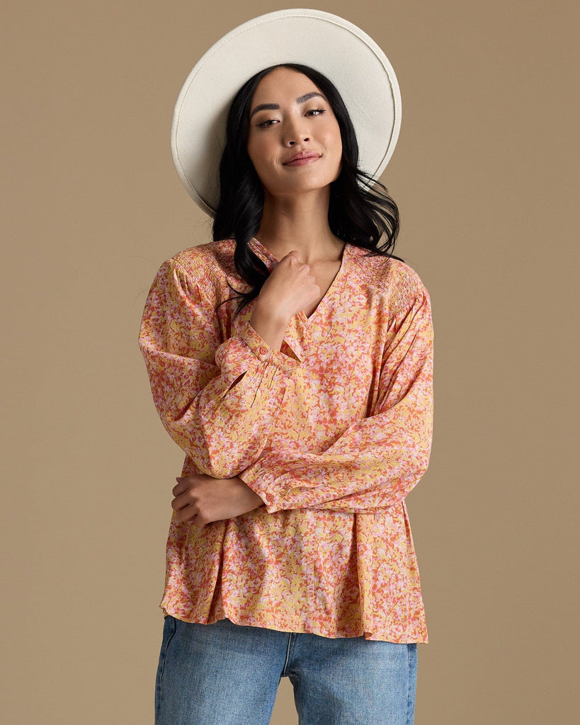 Woman in an orange, yellow and pink blouse with long sleeves