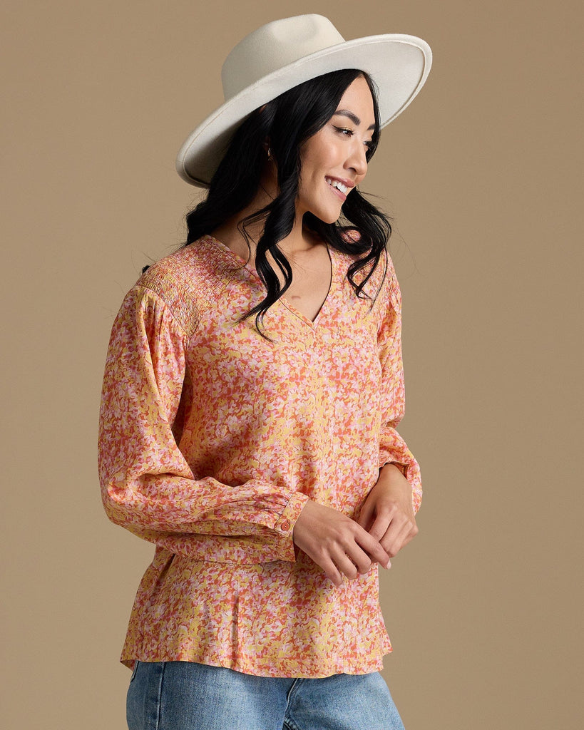 Woman in an orange, yellow and pink blouse with long sleeves