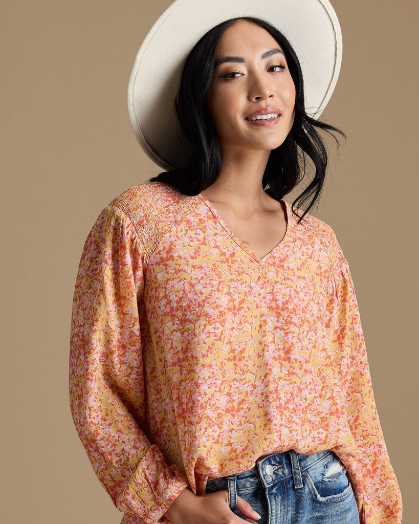 Woman in an orange, yellow and pink blouse with long sleeves