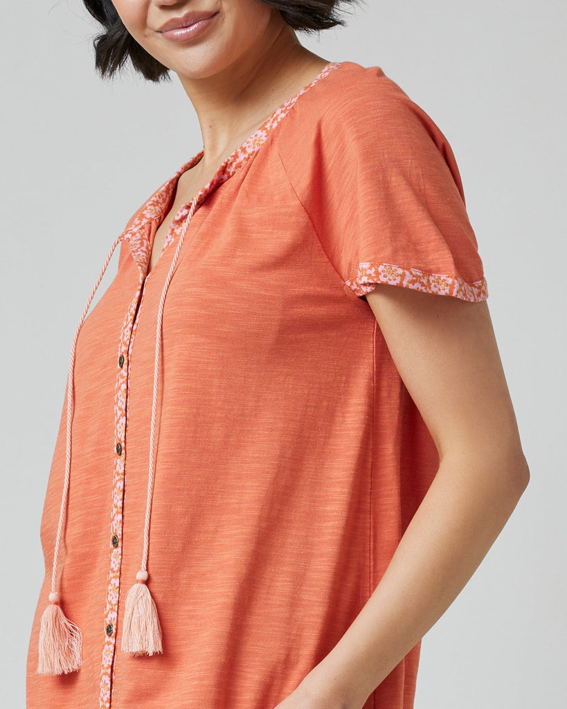 Woman in an orange top with short sleeves and buttons down the front