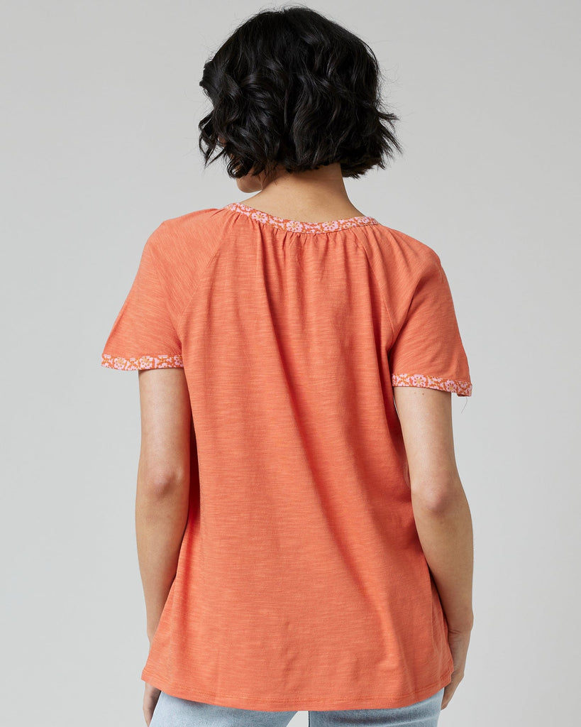 Woman in an orange top with short sleeves and buttons down the front