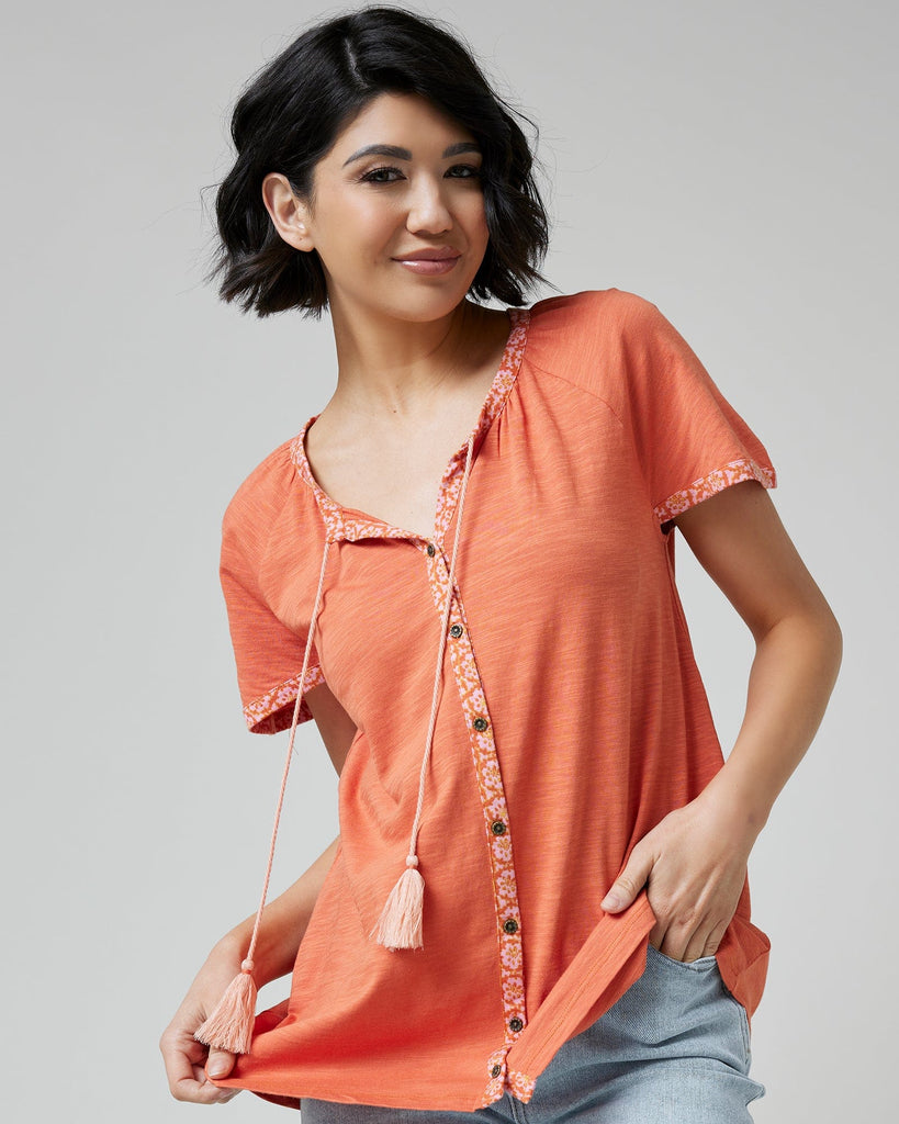 Woman in an orange top with short sleeves and buttons down the front