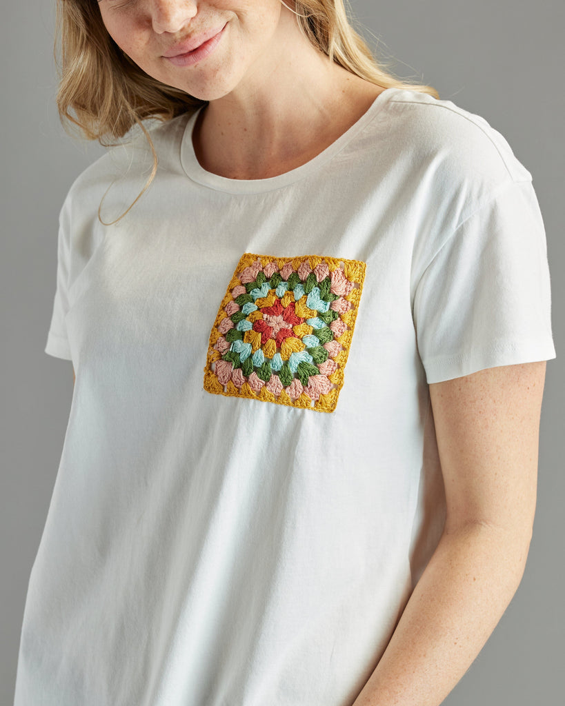 Woman in a white t-shirt with short sleeves and a crochet patch on chest