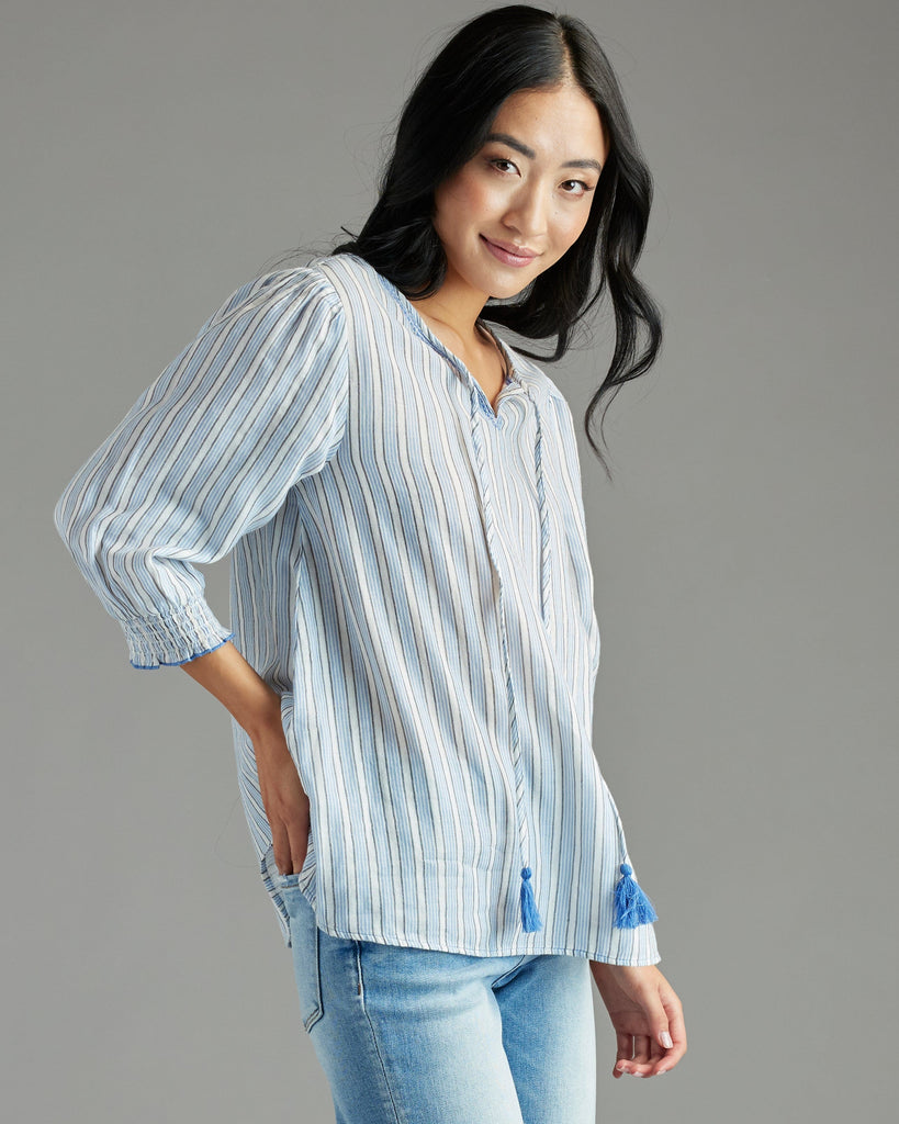 Woman in a blue blouse with 3/4 length sleeves, vertical stripes and tassels