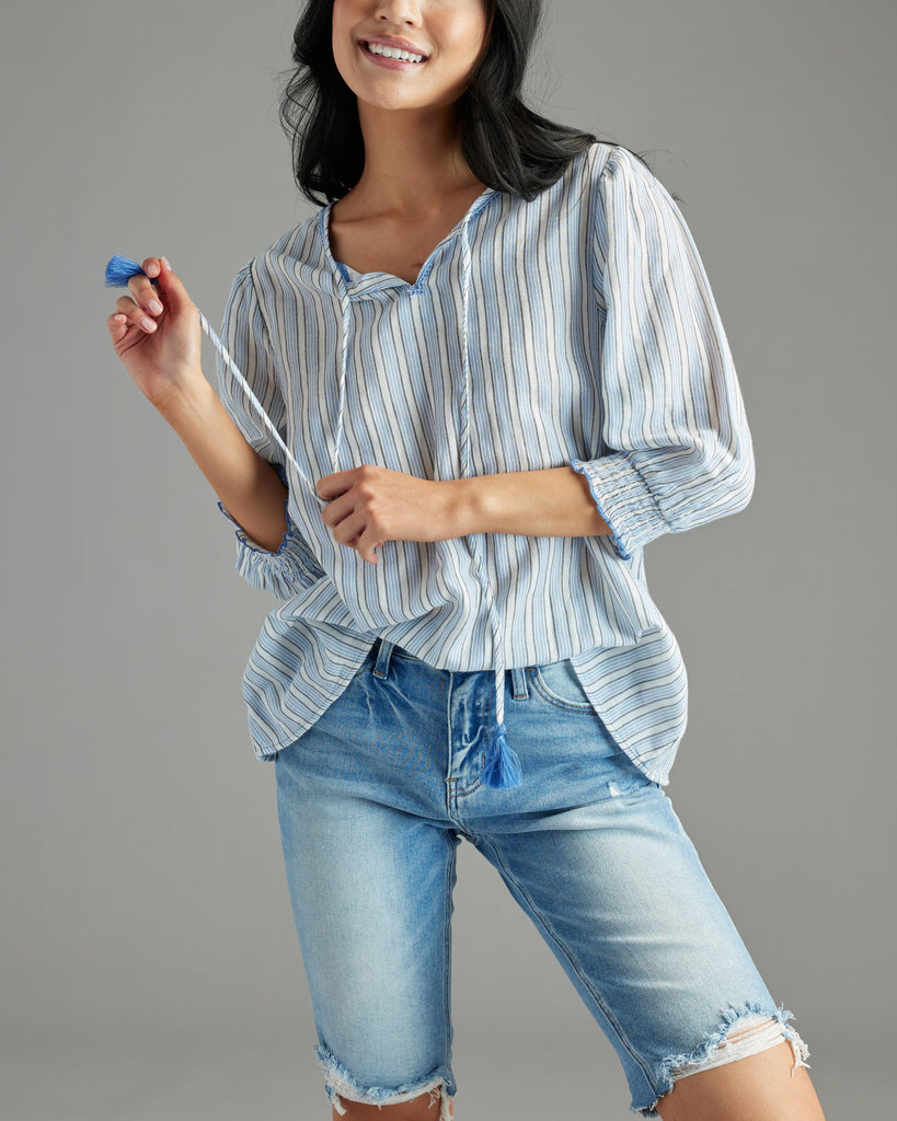 Woman in a blue blouse with 3/4 length sleeves, vertical stripes and tassels