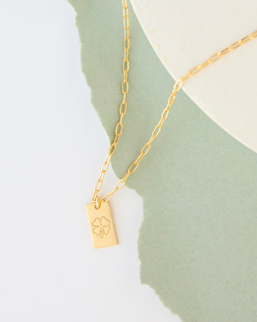 Gold necklace with four leaf clover on charm.