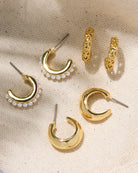 Set of gold hoop earrings with pearl accents on a beige fabric background