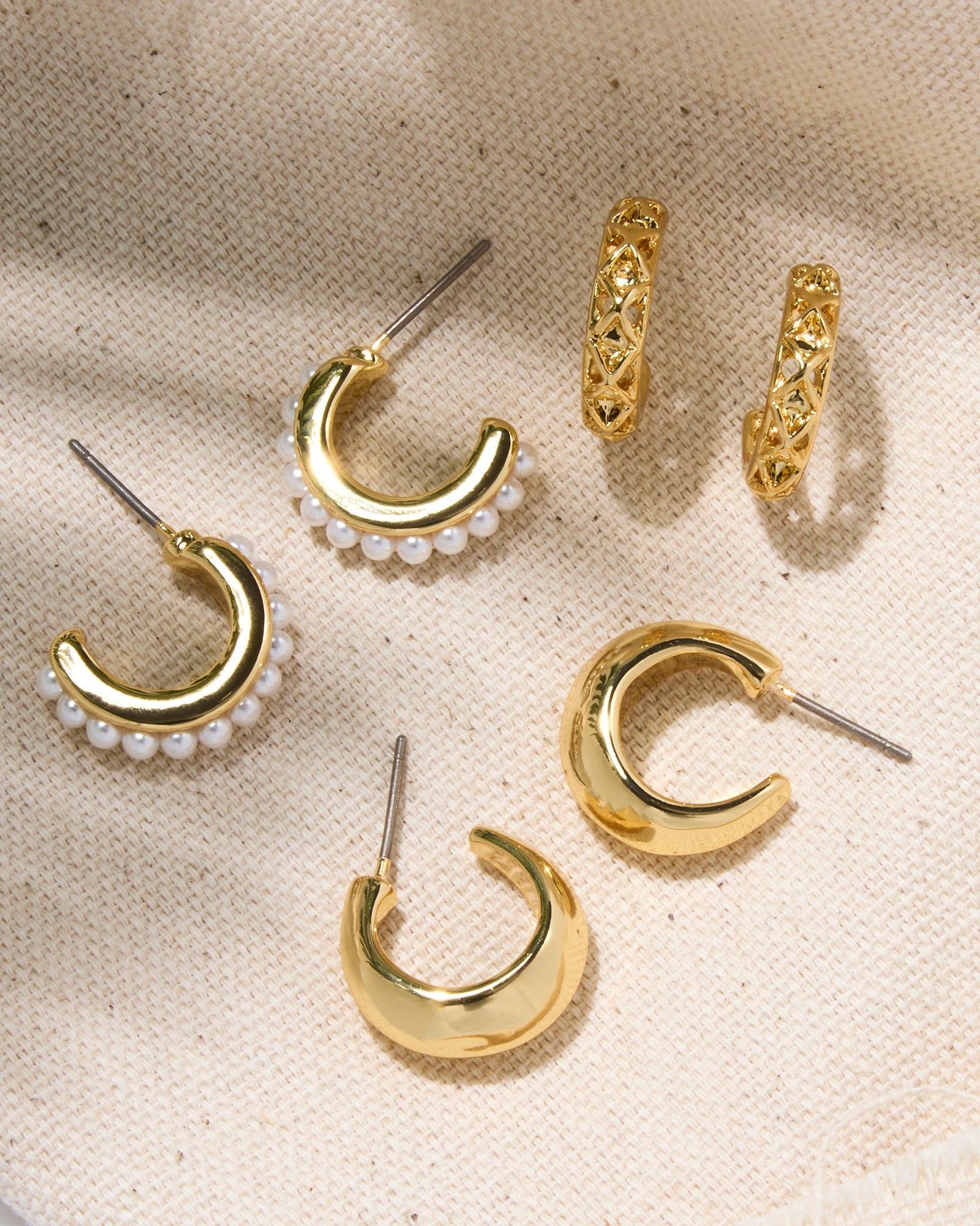 Set of gold hoop earrings with pearl accents on a beige fabric background