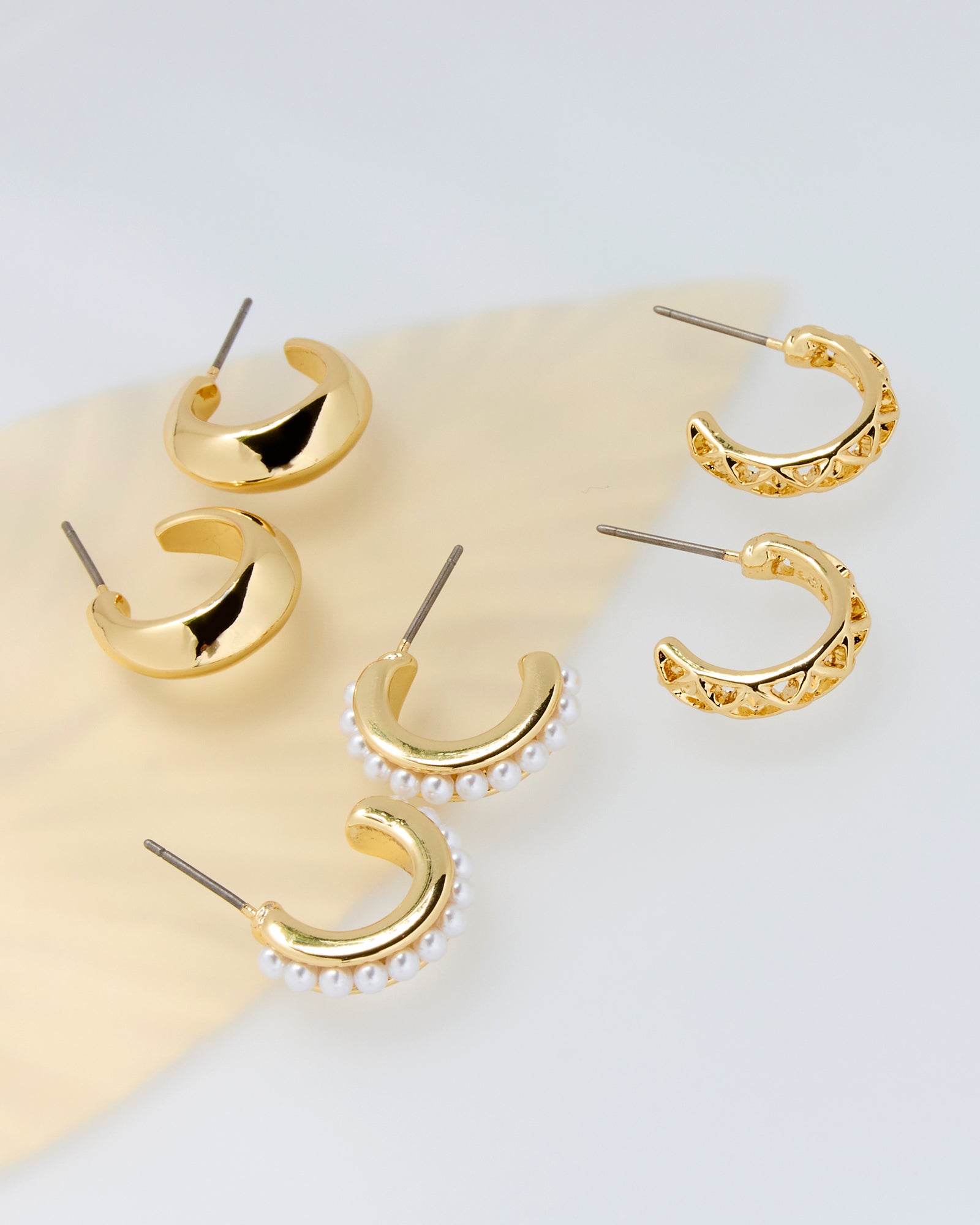 Set of gold hoop earrings with pearl accents on a light background