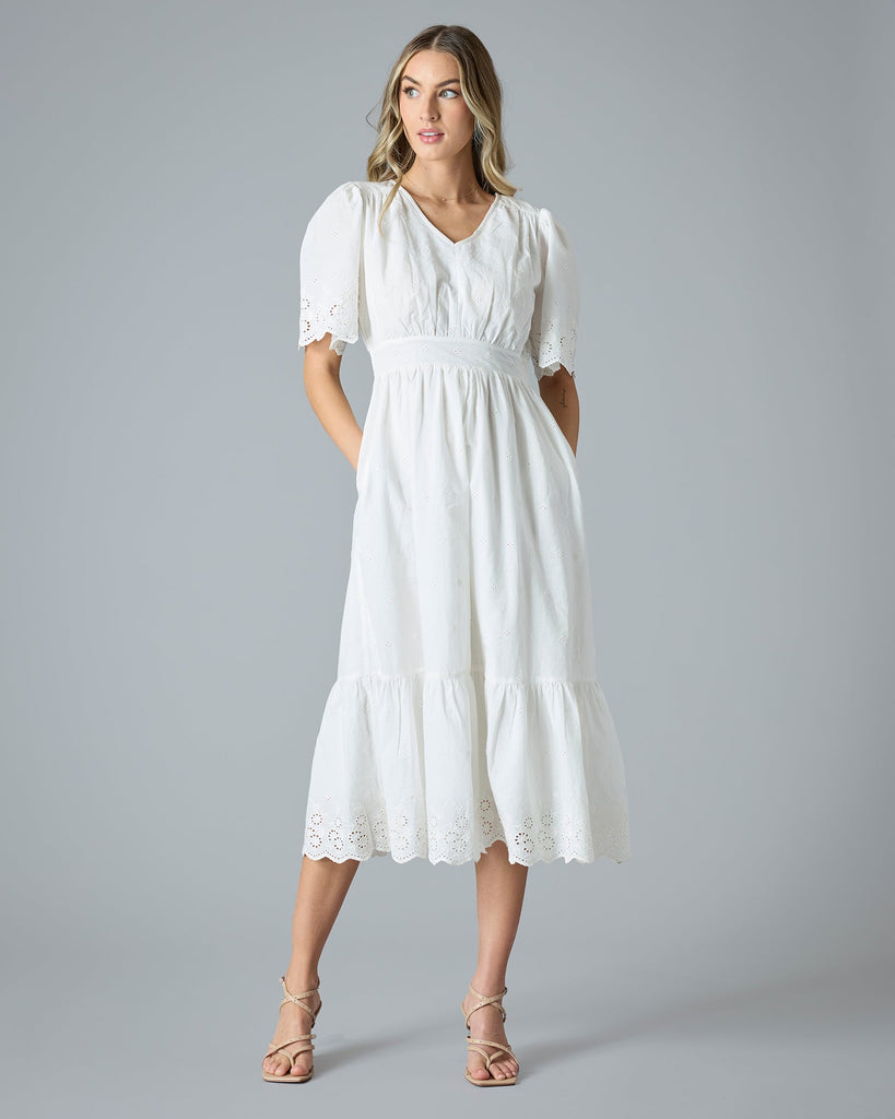 Woman in a white short sleeve, midi-length dress with eyelet details on hem