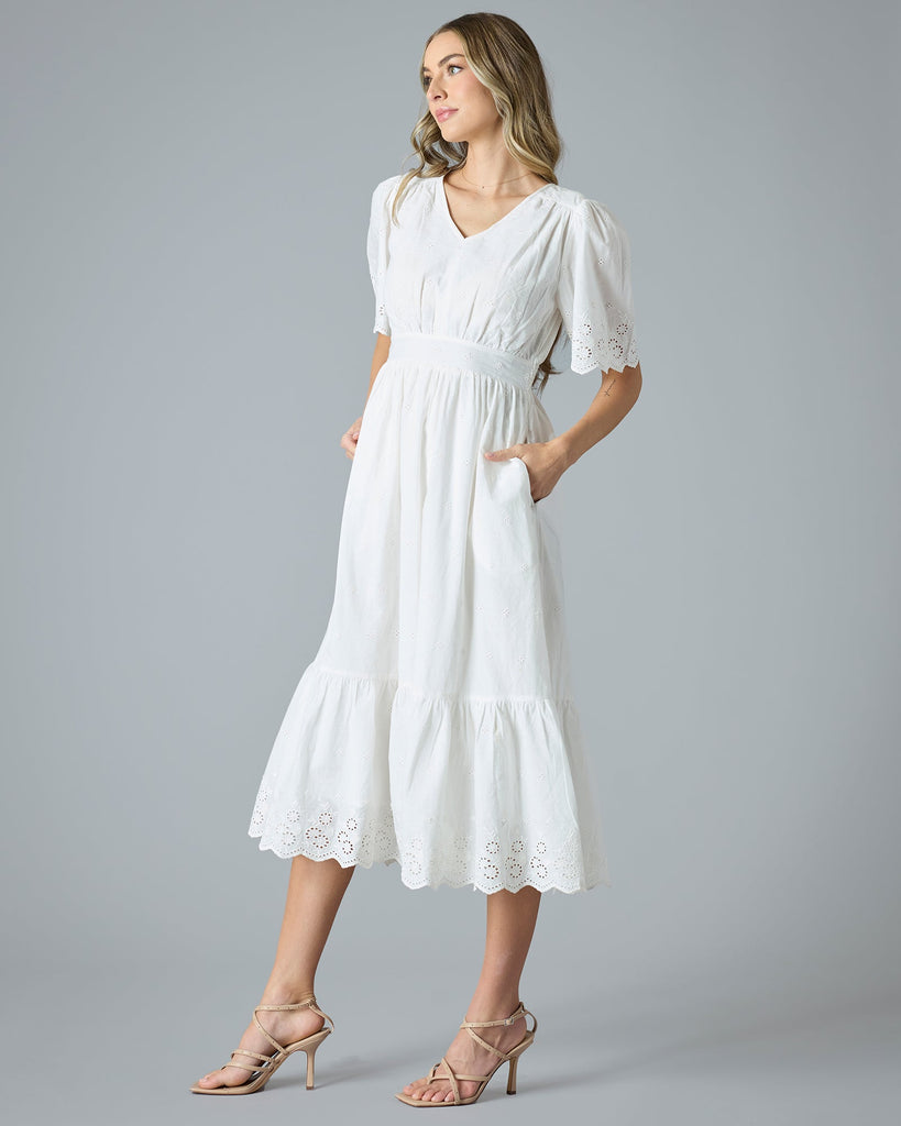 Woman in a white short sleeve, midi-length dress with eyelet details on hem