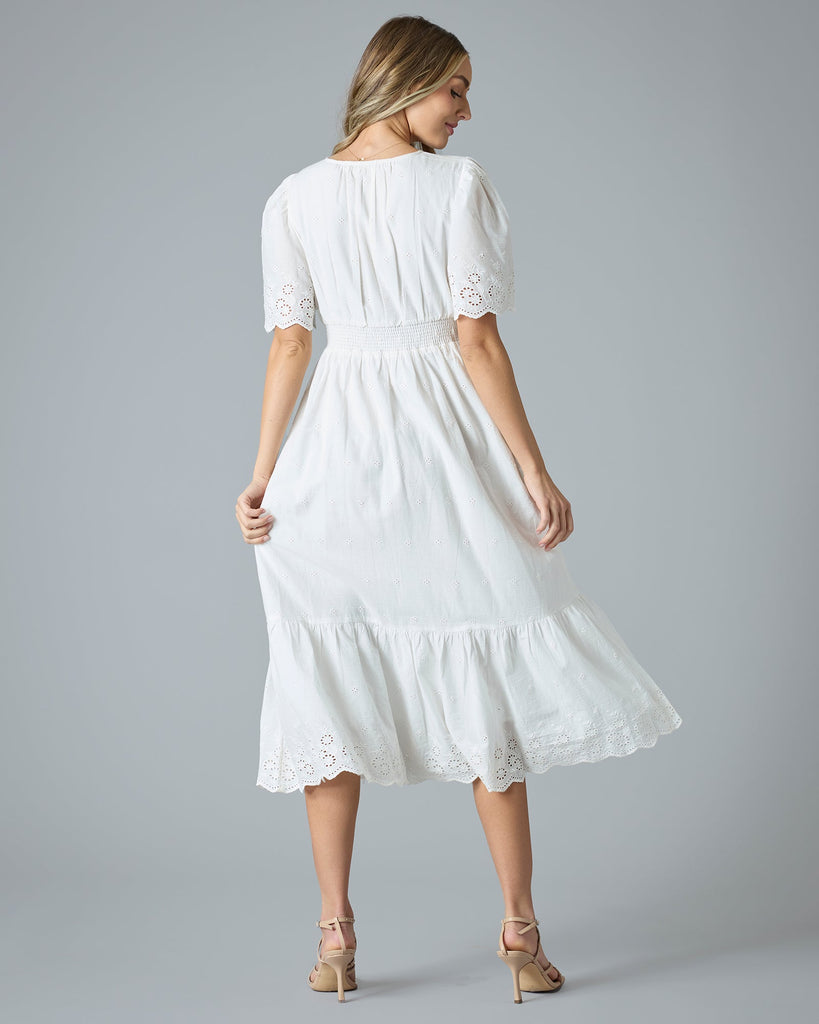 Woman in a white short sleeve, midi-length dress with eyelet details on hem