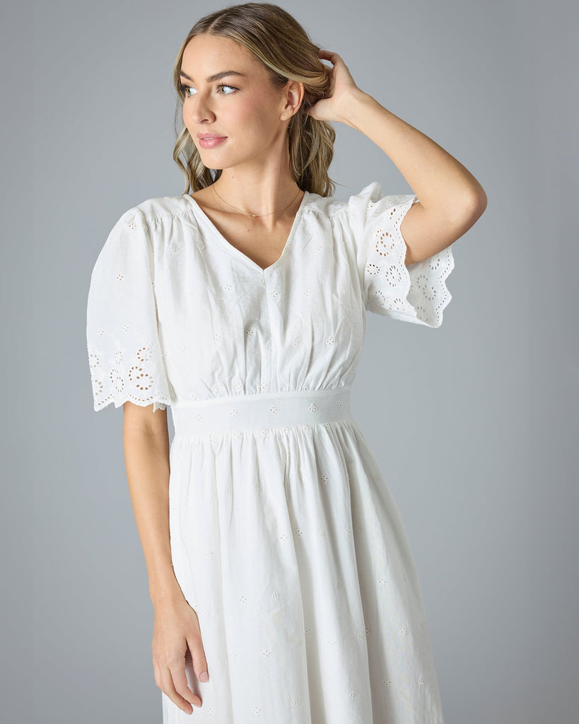 Woman in a white short sleeve, midi-length dress with eyelet details on hem