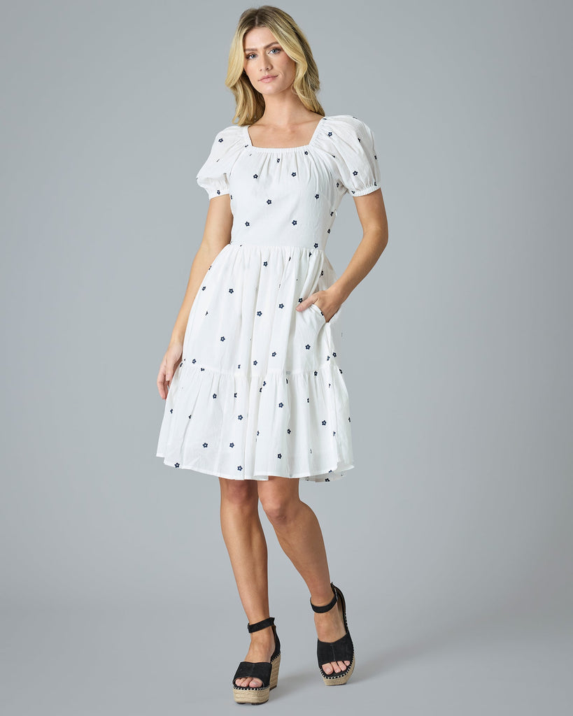 Woman in a white with blue flower dress that is knee-length and short sleeves