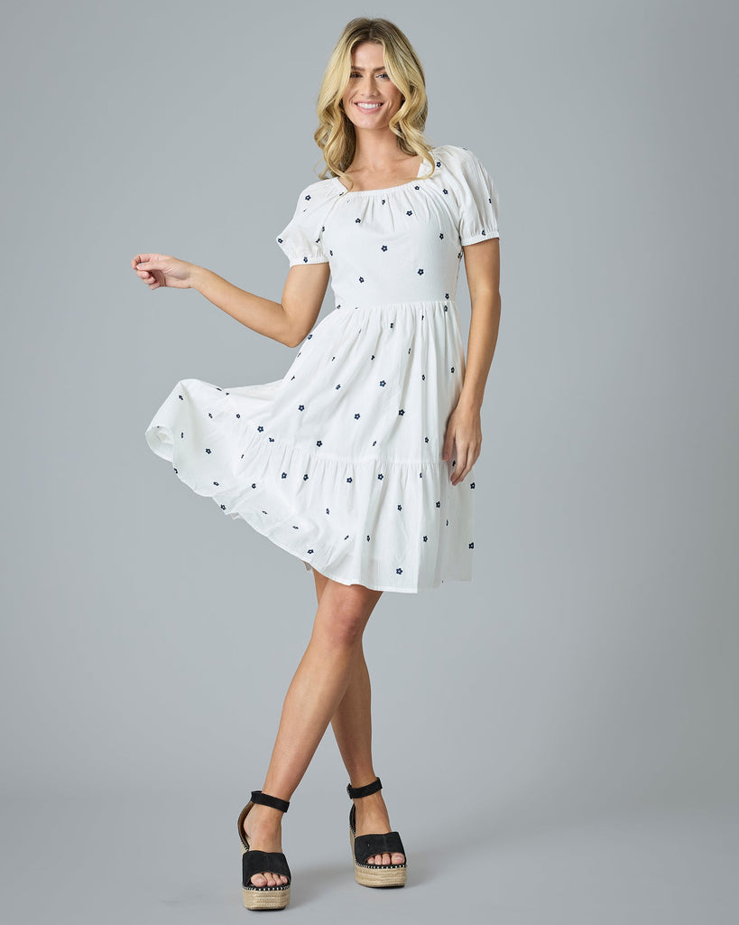 Woman in a white with blue flower dress that is knee-length and short sleeves