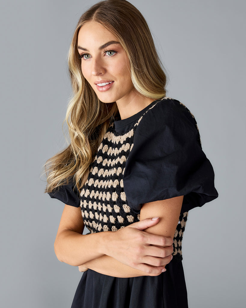 Woman in a black short sleeve, midi dress with non-attached sweater vest on top