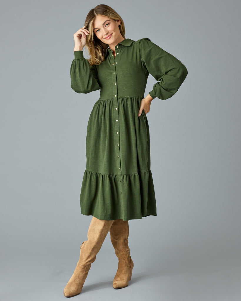 Woman in a green, long sleeve, collared, buttondown dress that is midi length