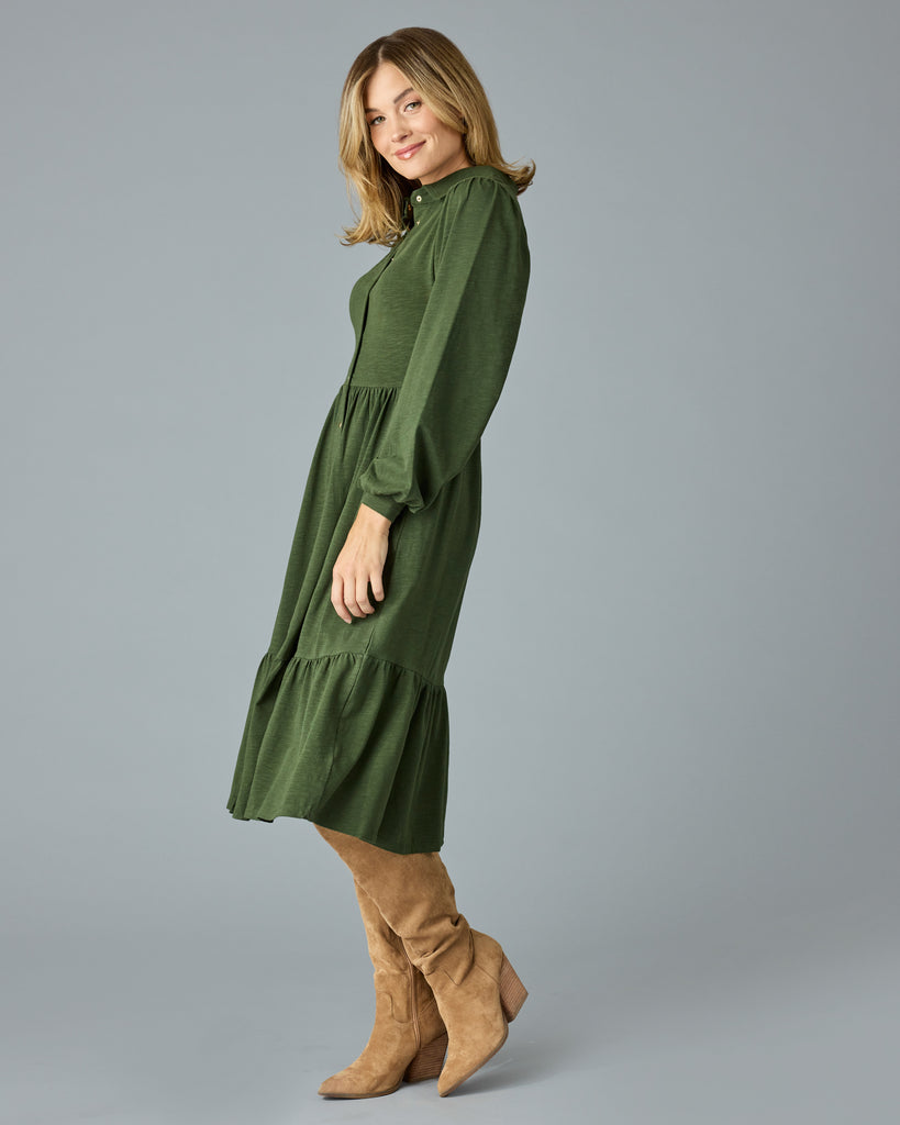 Woman in a green, long sleeve, collared, buttondown dress that is midi length