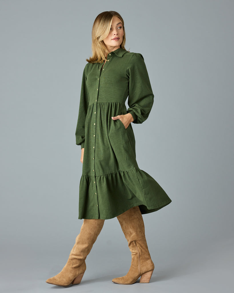 Woman in a green, long sleeve, collared, buttondown dress that is midi length