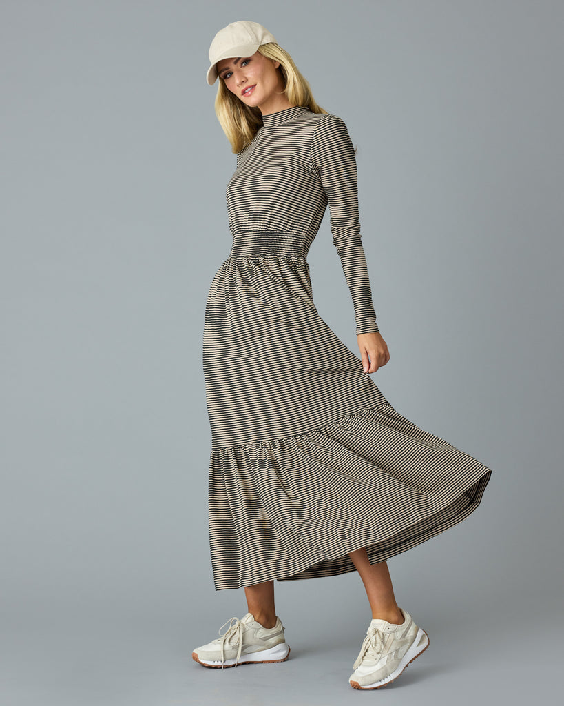 Woman in a black and tan thin striped maxi dress with long sleeves, a mock neck and pockets