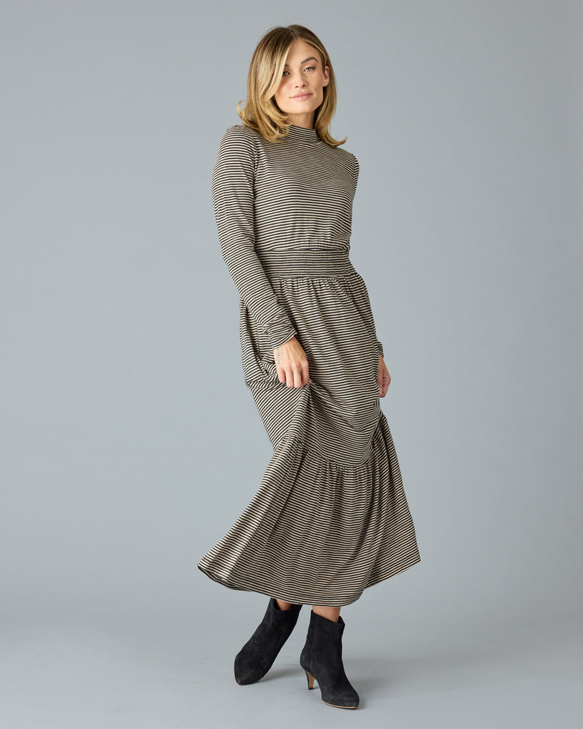 Woman in a black and tan thin striped maxi dress with long sleeves, a mock neck and pockets