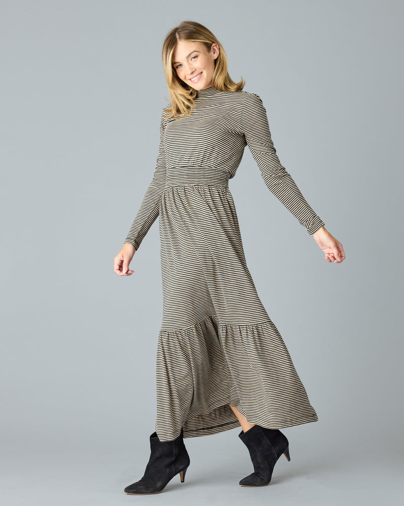 Woman in a black and tan thin striped maxi dress with long sleeves, a mock neck and pockets