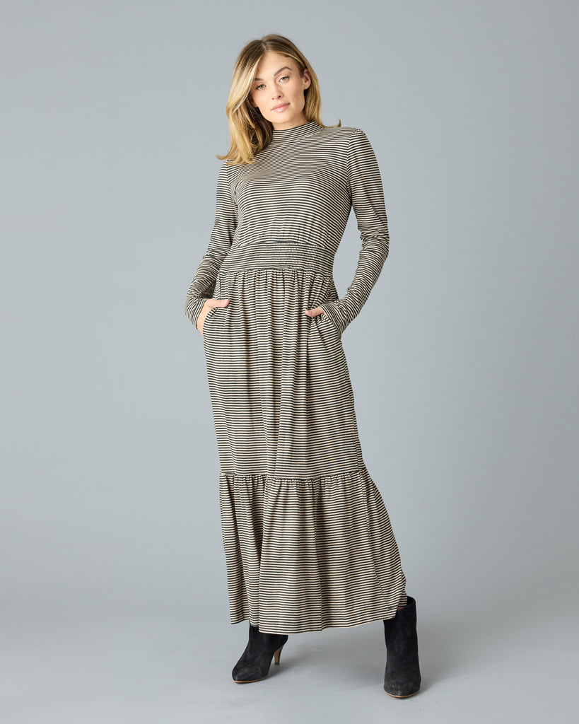 Woman in a black and tan thin striped maxi dress with long sleeves, a mock neck and pockets