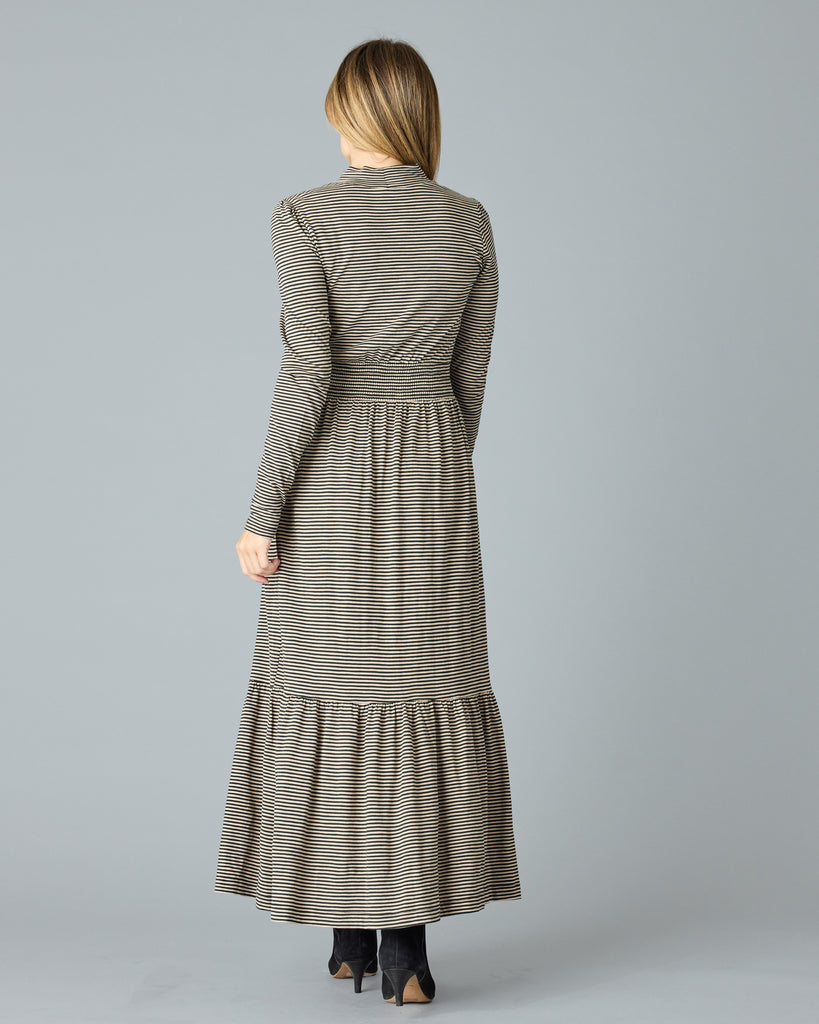 Woman in a black and tan thin striped maxi dress with long sleeves, a mock neck and pockets