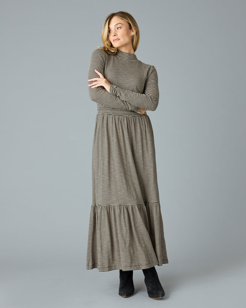 Woman in a black and tan thin striped maxi dress with long sleeves, a mock neck and pockets