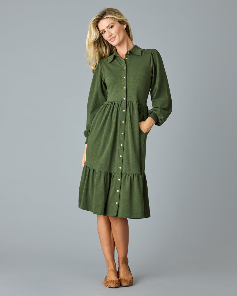 Woman in a green, long sleeve, collared, buttondown dress that is midi length