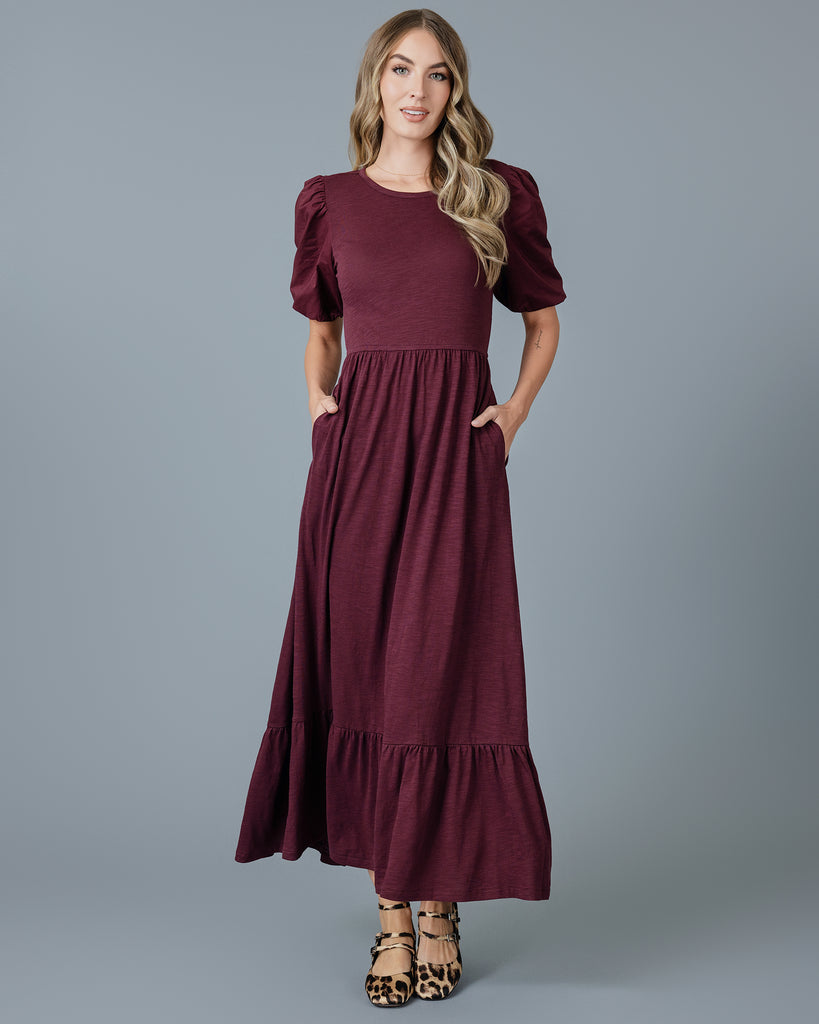 Woman in a plum colored short sleeve, maxi length knit dress