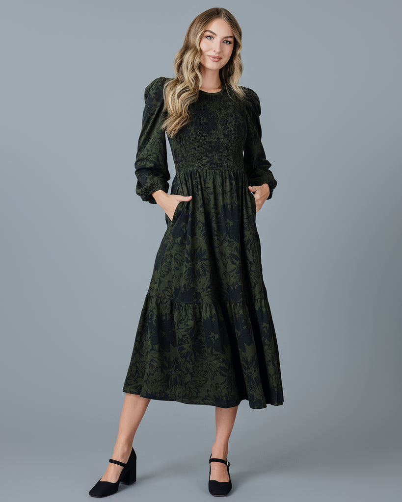 Woman in a green and black long sleeve knit midi-length dress with smocking on bodice