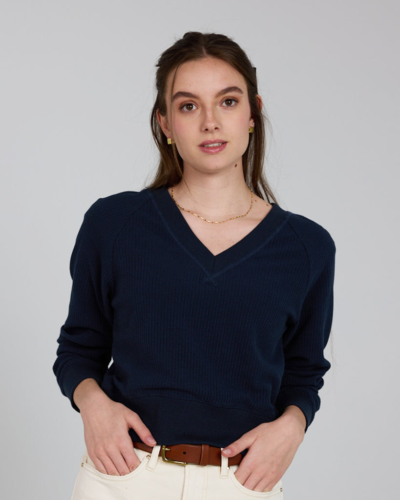 Model wearing a dark blue, v-neck, long sleeve waffle fabric pullover sweater.