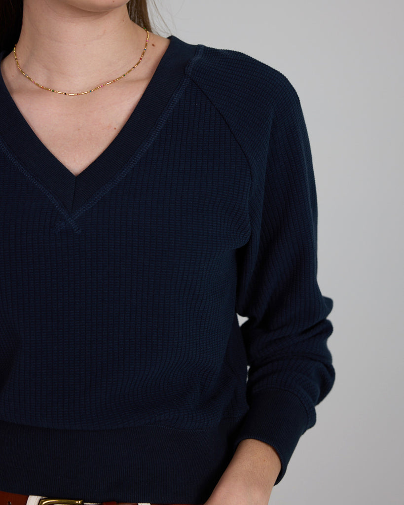 Model wearing a dark blue, v-neck, long sleeve waffle fabric pullover sweater.