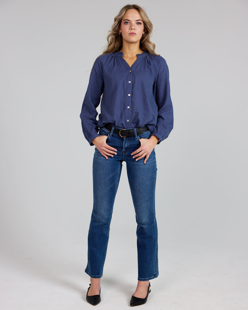 Model wearing a cobalt blue long sleeve v-neck blouse with button details down the front.