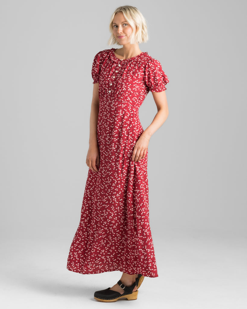 Model wearing a red with white floral print, short sleeve, round neck with ruffle details, maxi length slip dress.